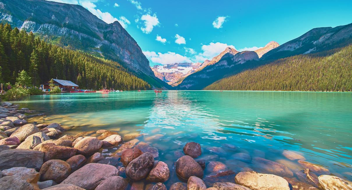 Lac turquoise aux eaux claires avec rochers en premier plan et montagnes enneigées en fond